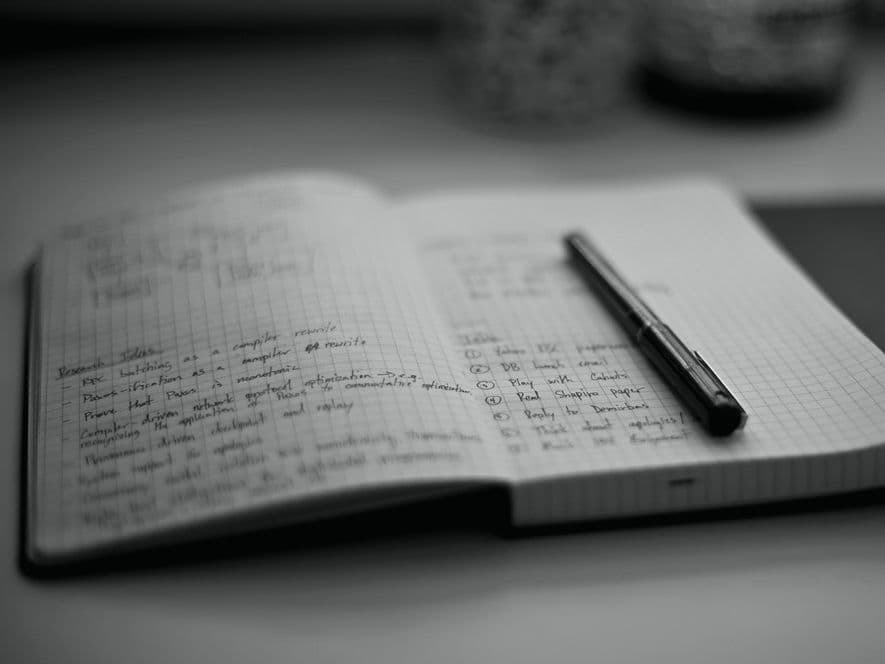 Un carnet ouvert de notes de recherche manuscrites à côté d'un stylo